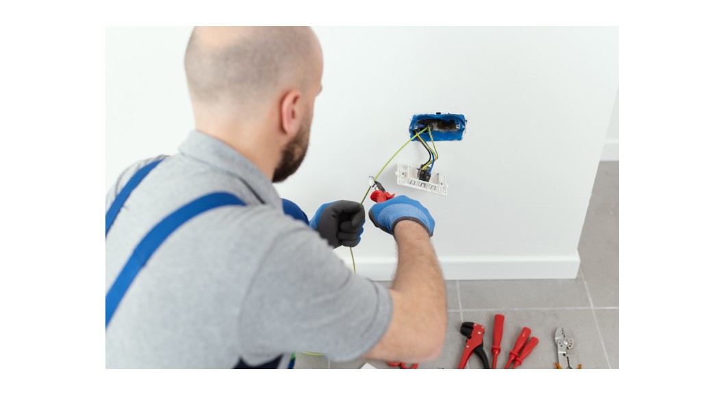 An electrician fixes a socket taking out the wires from behind the wall plate